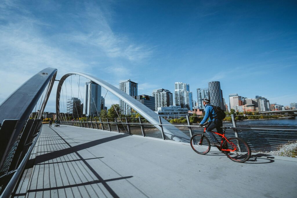 pexels-photo-11632841-11632841 A cyclist rides across a modern bridge with a city skyline in the background, under a clear blue sky.